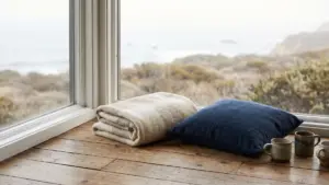 A bare wooden floor by a window with a folded blanket and a cushion
